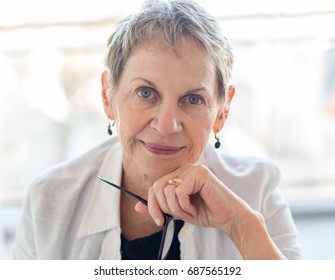 Close Up Of Professional Looking Older Woman With Short Grey Hair And Blue Eyes Holding Glasses (selective Focus)