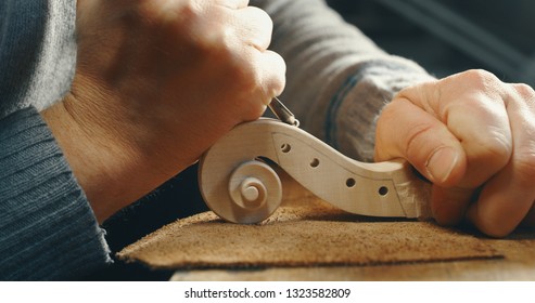 Close up of professional master artisan luthier painstaking detailed work on wood violin in a workshop.