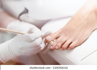 Close up of professional painting by white and glossy acrilyc paint nails on foot. Specialist in beauty salon making french pedicure for female client. Relaxing at beauty salon, caring about nails.