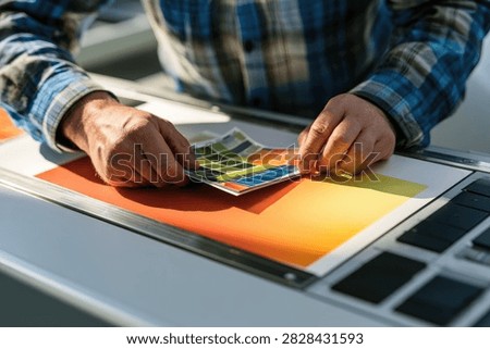 Close up of a professional printer hands checking color quality control on printed paper samples at a printing house offset press machine.
