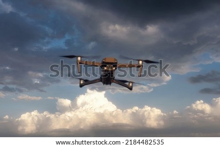 Close up of professional remote control drone flying against dramatic sky background at sunset.