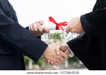 Close up Professor handshake of graduate congratulations celebrating with sending a roll of giving diplomas certificate in hand and feeling so happiness in Commencement day. success education concept.