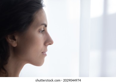 Close Up Profile Face View Of Hispanic Sad Woman Standing Indoor, Looks Out Window, Deeply In Mournful Thoughts Feels Depressed Experiencing Life Troubles. Cheerless Female Portrait, Problems Concept