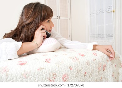 Close Up Profile Portrait Of An Attractive Young Woman Laying Down On Her Bed Relaxing At Home And Having A Telephone Conversation. Home Interior Lifestyle.