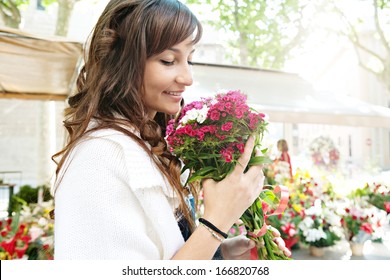 Close up profile portrait of a beautiful and young woman enjoying and smelling a bouquet of flowers while standing in a fresh floral market stall during a sunny day outdoors. - Powered by Shutterstock