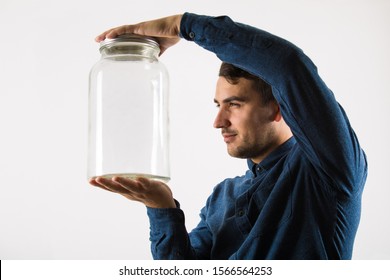 Close Up Profile Portrait Of A Curious Businessman Holding An Empty Glass Jar In His Hands Looking With Sneaky Eyes Isolated Over White Background.