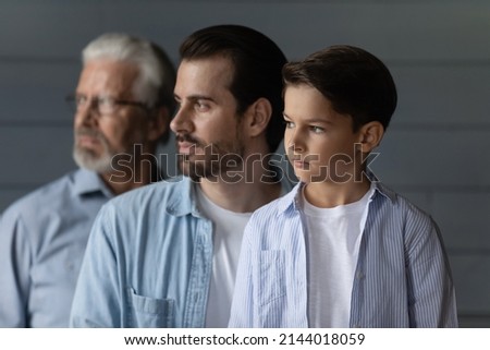 Close up profile three generations of men standing in row on grey studio wall background, looking in distance, serious 7s boy with father and senior grandfather dreaming, visualizing future