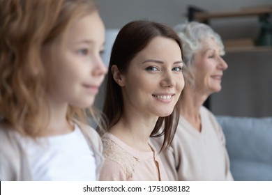 Close up profile view of three generations of women look in distance dreaming or visualizing, smiling young Caucasian mother look at camera, girl with mom and grandmother show family unity and bonding