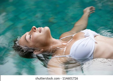 Close up profile view of a young woman floating in water while in a swimming pool on vacation.