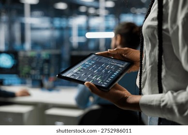 Close up of programmer in data center using tablet, managing AI training datasets. IT employee using device to oversee machine learning in server farm supporting scalable infrastructure for AI apps