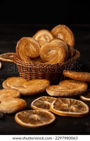 Close up of puff pastry in basket on dark table with dried oranges, selective focus, black background, vertical with copy space
