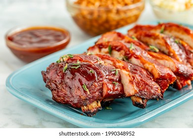 Close Up Of Rack Of Bbq Smoked Ribs Sliced On Bright Blue Plate With Sides Of Cole Slaw And Backed Beans In Background And Bowl Of Sauce