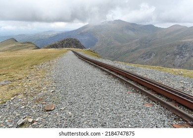 Close Up Of Railway Train Tracks Going Into Distance On Top Of Snowdonia, Wales Mountain Range On A Cloudy Spring Day