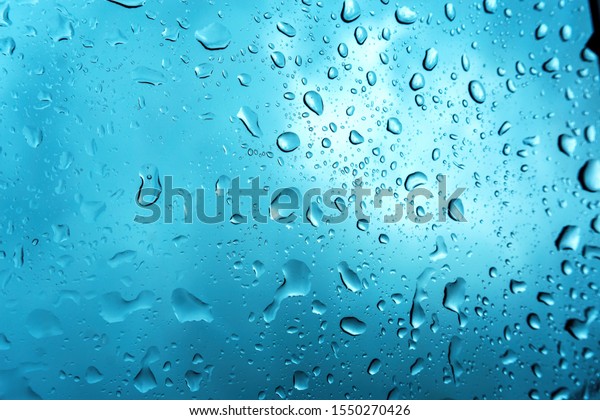 Close up rain\
droplets on car windshield over blurred blue sky, rainy season\
abstract water drops background.\

