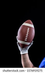 Close up of the raised hand of a Caucasian male American football player wearing a glove and holding a football in the air. Vertical shot