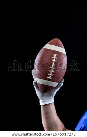 Close up of the raised hand of a Caucasian male American football player wearing a glove and holding a football in the air. Vertical shot