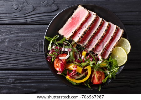 Close up of rare seared Ahi tuna slices with fresh vegetable salad on a plate. Top view from above horizontal
