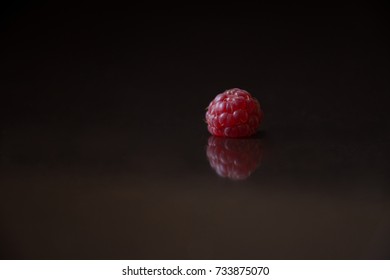 Close up of a raspberry resting on a black surface upside down. It's reflection is visible. Photographed with a shallow depth of field. 