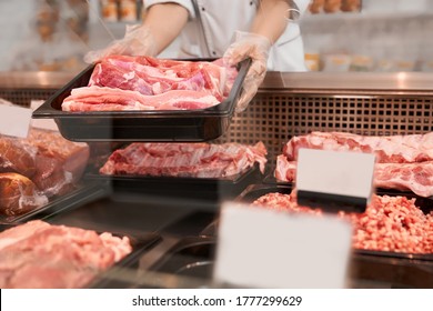 Close up of raw meat pieces in refrigerator with price tags ready for sale in meat department of store. Female hands putting out of glass counter plate with sliced fresh steaks. Concept of food. - Powered by Shutterstock