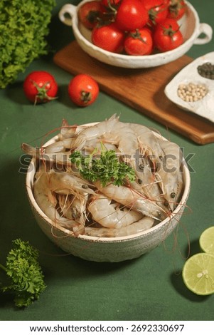 Close up Raw Shrimp piled in rustic bowl. Parsley garnish. Tomatoes, lime, and spices in background on dark green surface. Fresh seafood display. Vertical shot
