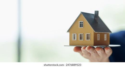 Close up real estate agent holding small house model, Home loan. - Powered by Shutterstock