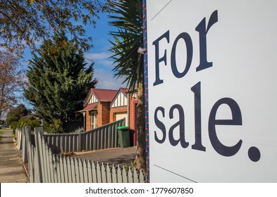 Close up of a real estate sign board with text  'for sale' , some suburban houses/Australian homes and pedestrian walkway as background. Concept of selling property and real estate market/investment.