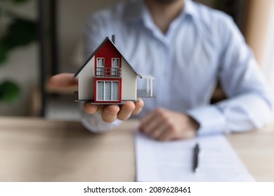 Close up realtor sit at table holds tiny house model, layout of cottage. Real estate purchase, new property, ownership, construction company make special offer to client, affordable dwelling concept