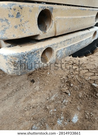 Close up of rear counterweights and chassis frame with bolt holes on yellow backhoe loader. Heavy construction equipment detail, industrial machinery and maintenance concept.