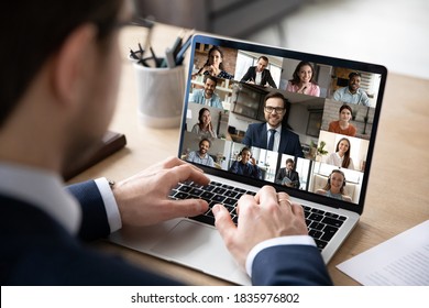Close up rear view businessman engaged in online conference, using laptop, sitting at desk, diverse colleagues business people on computer screen, negotiations, briefing, employee making video call - Shutterstock ID 1835976802