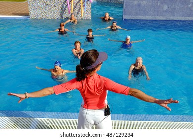 Close up rear view of fitness trainer at senior health class session in outdoor swimming pool. - Powered by Shutterstock