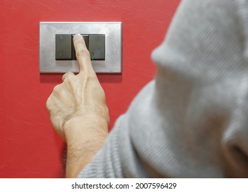 Close Up Rear View Left Hand Finger Young Man Turn Off Grey Light Switch On Leather Red Wall Decoration Before Going To Bed. Eco-friendly At Home And Electricity Bill Saving Concept. Selective Focus.