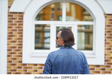 Close Up Rear View Of A Man Standing Alone In Front Old Town Building Looking Sideways While Traveling In European Cities During Vacation Time Wearing Denim Jeans Shirt. Travel Concept. 