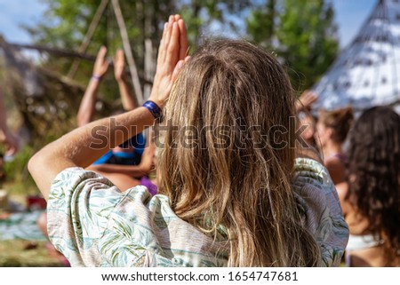 A close up and rear view in selective focus of a thirty year old man with blonde hair and hands in prayer position, Anjali Mudra, Namaste at earth festival
