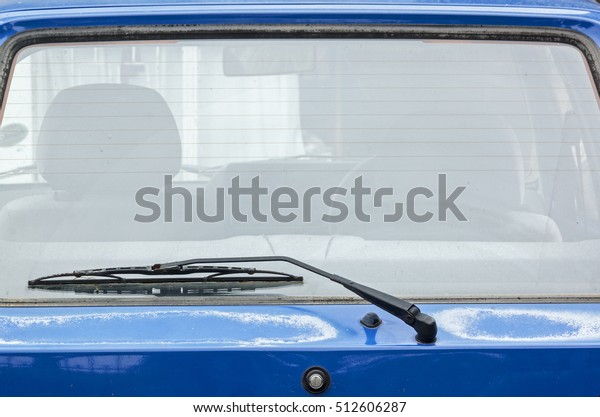 Close up of rear windshield wiper\
arm and blade on sun bleached blue vintage motor\
vehicle