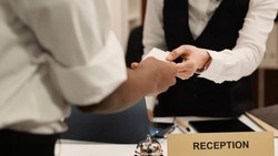 Close Up Of Receptionist Handing Card Key To Elegant African American Tourist During Check In Process. Business Travelling Guest Ready To Enjoy Hotel Stay After Receiving Room Access