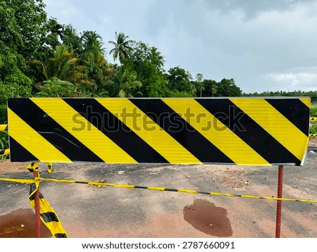 Close up of a rectangular yellow and black diagonal striped construction barricade on a rural roadside.