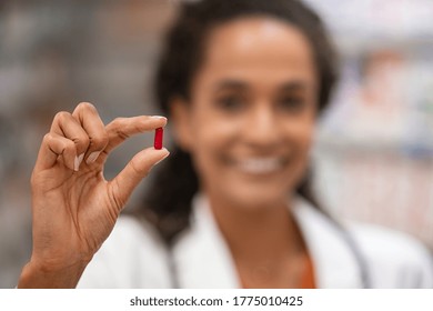 Close up of red analgesic pill held in the hand of a mixed race pharmacist. Smiling african woman pharmacist holding medicine. Close up hand of young woman doctor showing drug. - Powered by Shutterstock