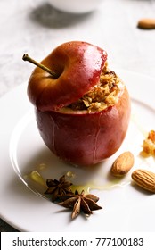 Close up of red baked apple with granola, cinnamon, nuts and honey on stone background. Healthy fruit dessert.
