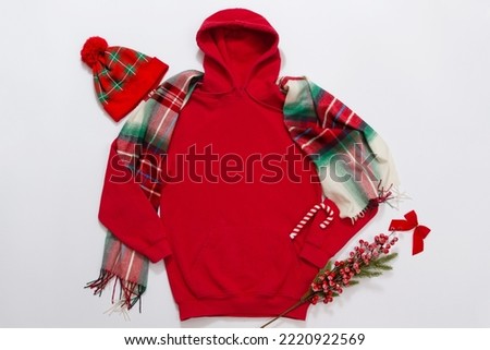 Close up red blank template hoodie copy space. Christmas Holiday concept. Top view mockup hoodie, scarf, hat. Red holidays decorations white background. Happy New Year accessories. Selective focus