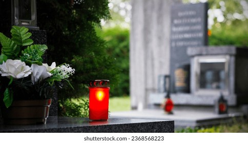 Close up of a red burning candle and flower decoration on the grave. Symbol of remembrance of our deceased relatives. Cemetery in the Czech Republic. All Souls' Day concept. All Saints Day