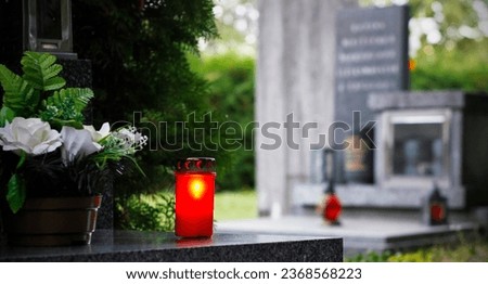 Close up of a red burning candle and flower decoration on the grave. Symbol of remembrance of our deceased relatives. Cemetery in the Czech Republic. All Souls' Day concept. All Saints Day