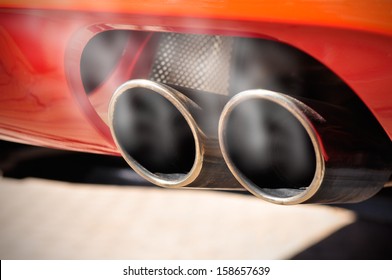 Close Up Of A Red Car Dual Exhaust Pipe With Smoke Around It