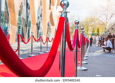 Close up red carpet ceremony with selective focus on the stanchions and the ropes with blurred guests and photographer background. Celebrity lifestyle concept. - Shutterstock ID 1095400145