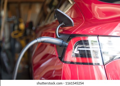 Close up of a red electric car's charge port plugged in and charging in a garage.