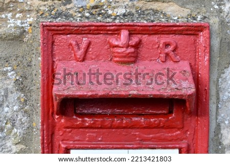 close up of red painted British Royal Mail letter box outside in a street,  showing the Queens crown and initials V R.  The post box is of British monarchy  Queen Victoria