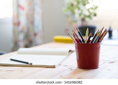 Close up of red tin bucket full of colorful color pencils and opened notebook with pencil on wooden table. Neat workspace at home. Early child development. - Powered by Shutterstock