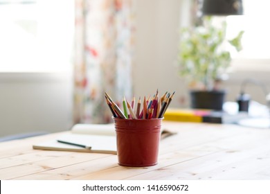 Close up of red tin bucket full of colorful color pencils and opened notebook with pencil on wooden table. Neat workspace at home. Early child development. - Powered by Shutterstock