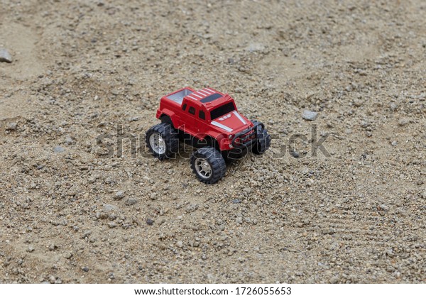 A close up of\
red toy car jeep in the sand