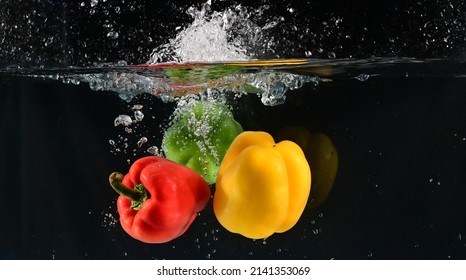 Close up of The red, yellow and green bell peppers fell into the water and the water splashed up with black background. Concept for health and vitamins.