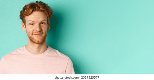 Close up of redhead bearded man looking pleased, nod in approval and smiling, standing in pink t-shirt against turquoise background.